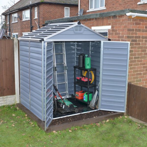 Grey plastic shed with a skylight, featuring double doors, a sloped roof, and interior shelving holding gardening tools and equipment, set in a backyard.