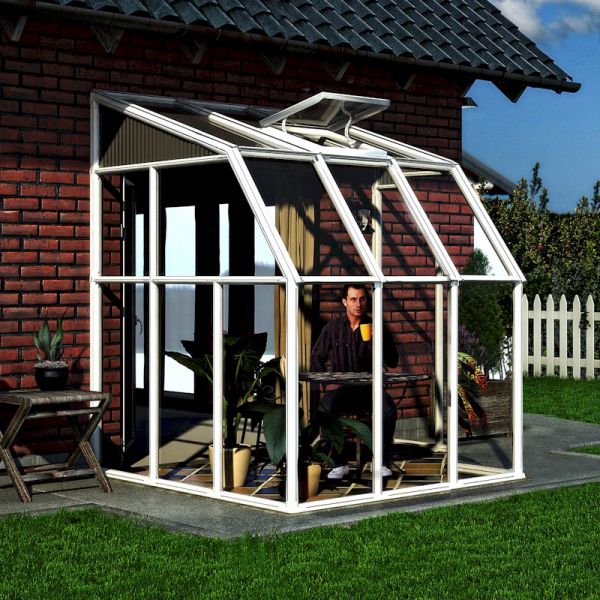 White, aluminum-framed lean-to sunroom with clear panels, featuring a sloped roof, large glass windows, and a door, set against a brick wall and garden.