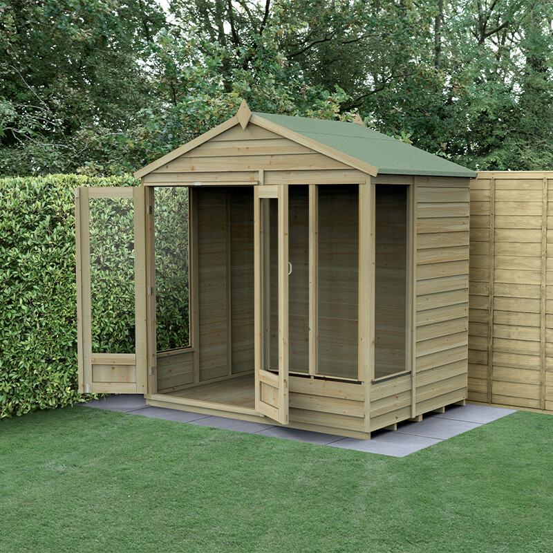 A wooden summer house with a double door, featuring a green apex roof, large windows, and a natural wood finish, set on a grassy area surrounded by hedges.