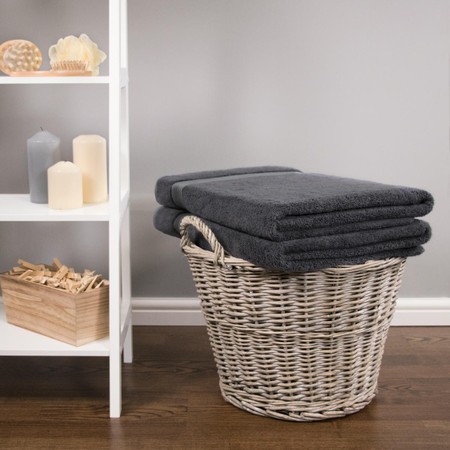Four dark grey bamboo charcoal bath sheets stacked neatly in a white wicker basket, alongside candles and decorative items on a shelf.