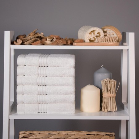White bamboo face cloths stacked neatly on a white shelf, accompanied by natural decor items like wooden pieces, candles, and a loofah, all against a gray background.