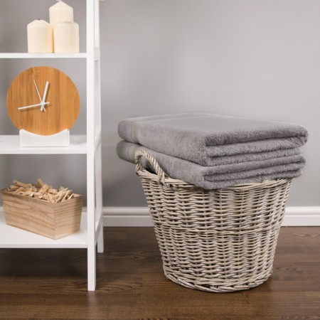 Light grey 700 GSM bamboo bath sheets stacked in a woven basket, beside a white shelf with candles and a wooden clock.