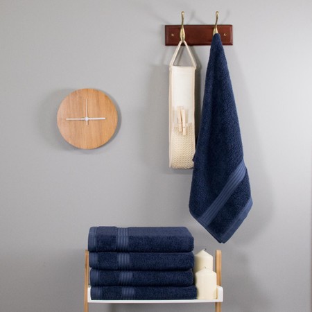 Navy blue 700 GSM bamboo hand towel hangs on a hook, with neatly stacked towels below, complemented by a wooden clock and decorative items in a modern setting.