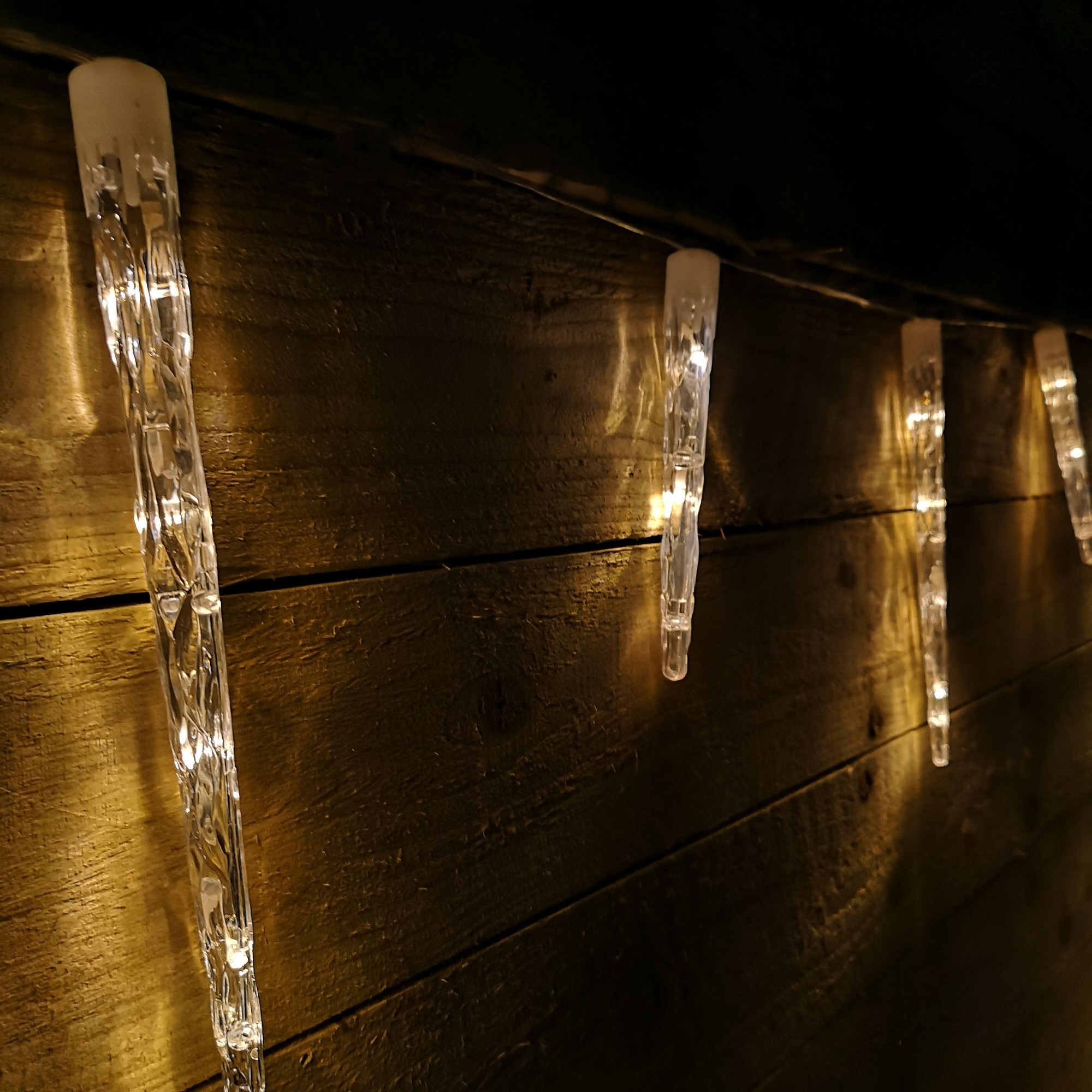 72 LED icicle-shaped Christmas lights in warm white, hanging from a wooden surface, featuring a chaser effect for a festive glow.