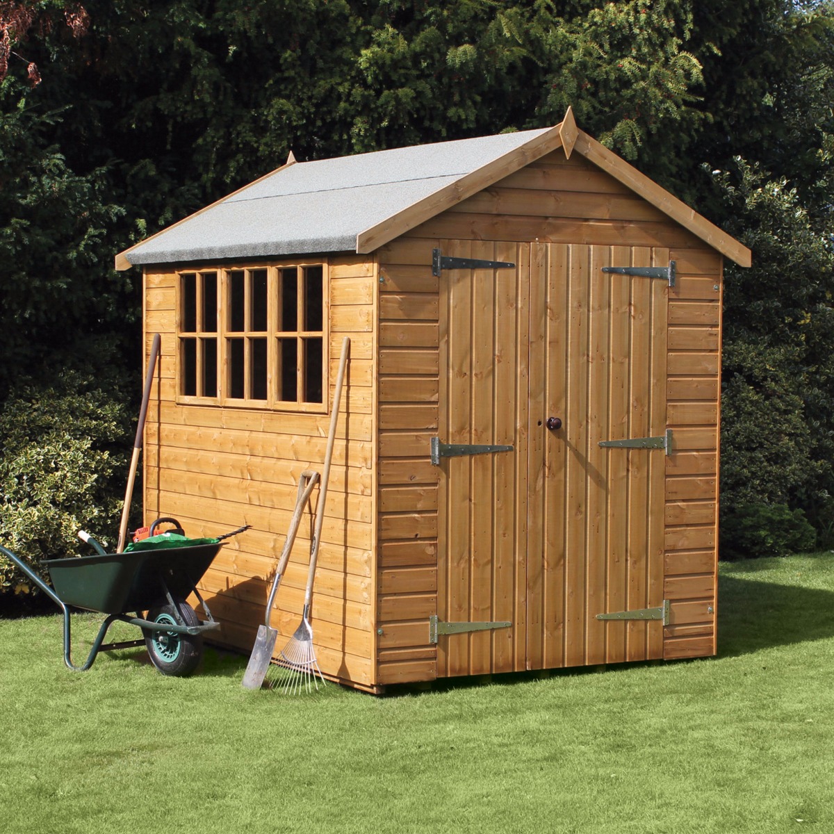Traditional heavy-duty shiplap wooden garden shed in natural wood finish, featuring a sloped roof, double doors with metal hinges, and a window, surrounded by gardening tools and a wheelbarrow.