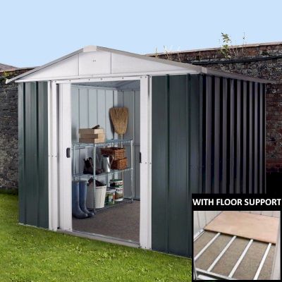 Green metal shed with a peaked roof, featuring double doors and shelves inside, set against a brick wall and grass, showcasing its spacious interior and sturdy construction.