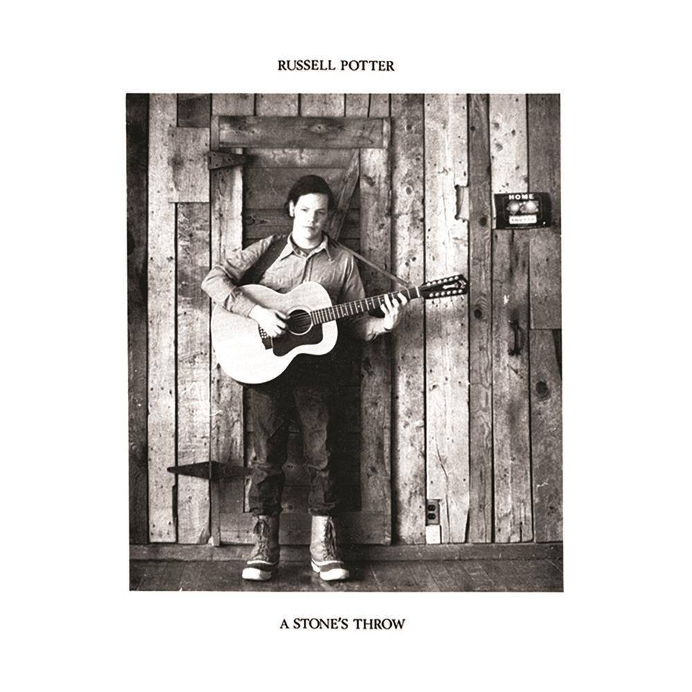 Black and white album cover featuring a man with a guitar, standing against a wooden wall, wearing a sweater and boots, with the title "A Stone's Throw" prominently displayed.