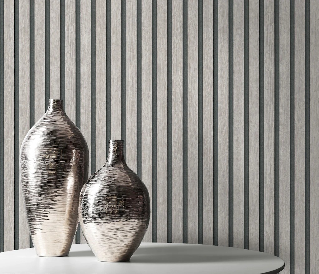 Textured wallpaper in 3D wood effect with vertical stripes in soft grey tones, complemented by two metallic vases in silver on a round white table.