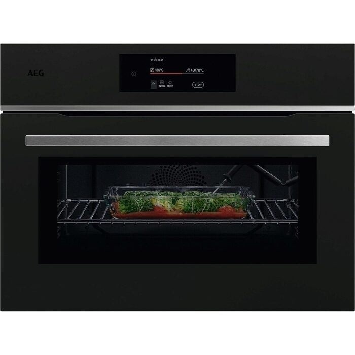 Matte black built-in combination microwave oven with a sleek stainless steel handle, digital display, and a glass door showcasing a dish with fresh vegetables inside.