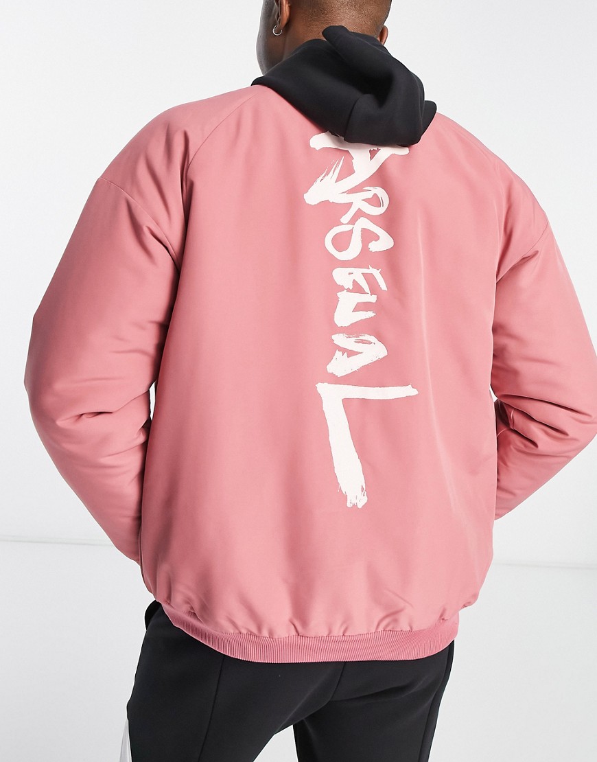 Padded jacket in soft pink with a black hood, featuring bold white "ARSENAL" lettering on the back and elastic cuffs for a snug fit.