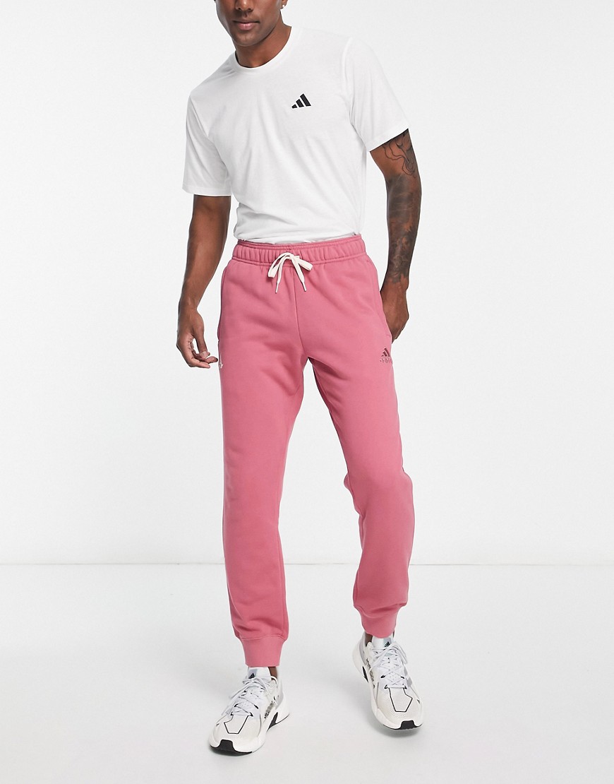 Pink calligraphy pants by Arsenal, featuring a relaxed fit, elastic waistband with drawstring, and side pockets, paired with a white t-shirt and sporty sneakers.