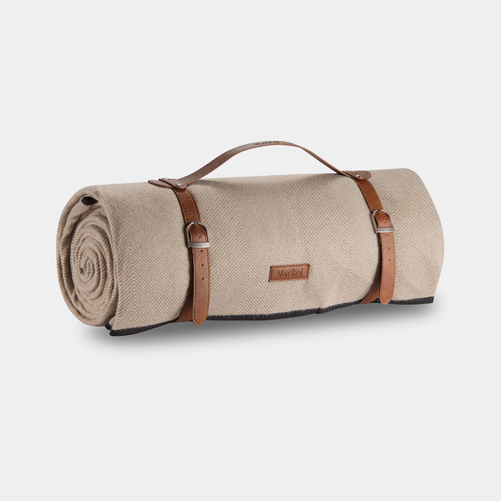 Beige waterproof picnic blanket, extra large, features a herringbone texture, rolled design secured with brown leather straps, and a dark trim along the edges.