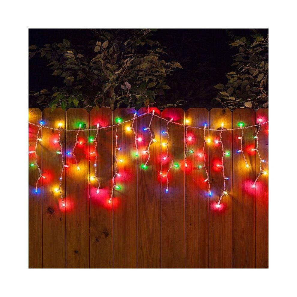 Multi-coloured outdoor connectable icicle lights with red, green, blue, and yellow bulbs hanging from a wooden fence, creating a festive glow against a night backdrop.