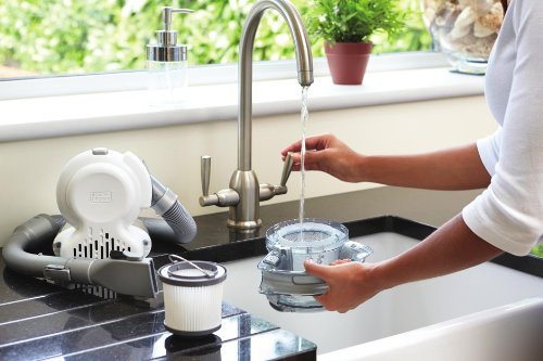 Black & Decker 0.56L 18V Li-Ion Dustbuster Flexi Handheld Vacuum in white and gray, featuring a flexible hose, removable filter, and compact design, placed next to a sink with running water.