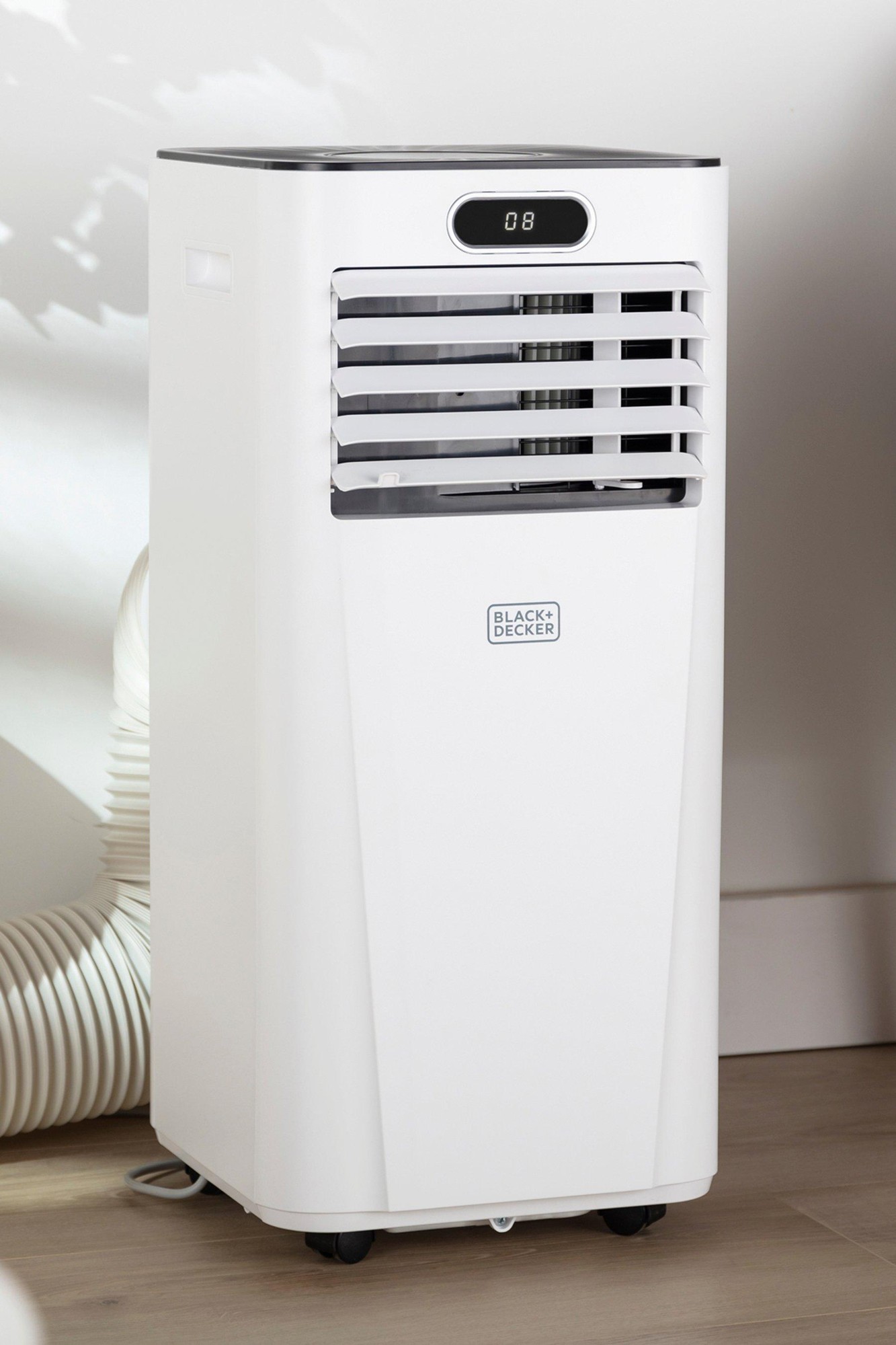 White portable air conditioner with a sleek design, featuring a digital display, adjustable vents, and wheels for mobility, labeled with the Black + Decker logo.