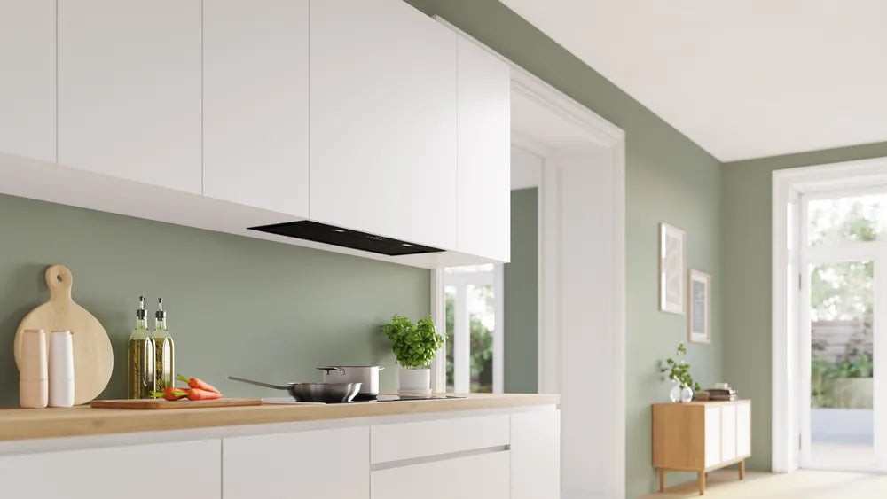 Bosch DLN87AC60B Series 6 86cm black canopy chimney hood mounted under white kitchen cabinets, with a wooden countertop featuring cooking utensils and ingredients.