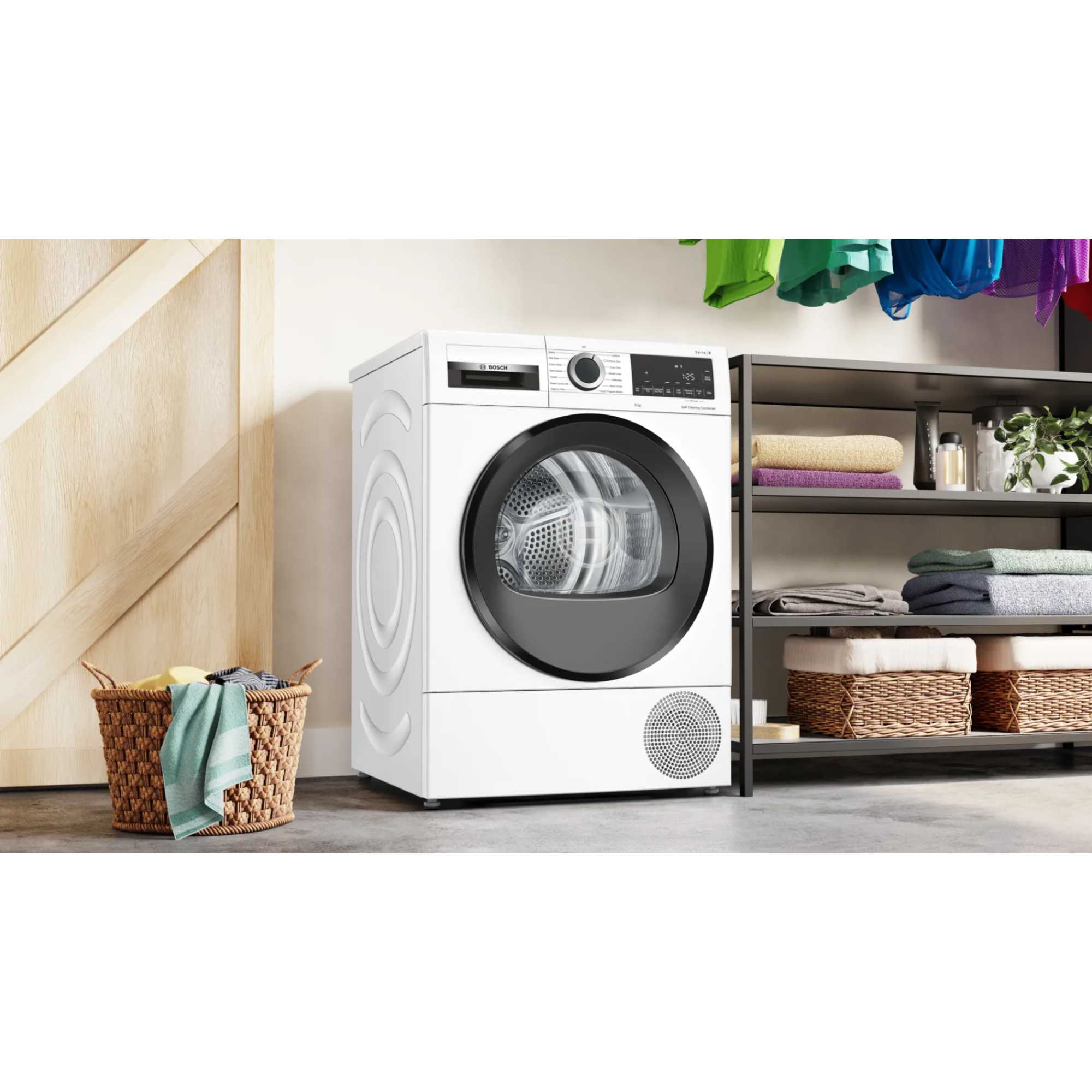White Bosch WQG245A0GB heat pump tumble dryer with a large glass door, digital display, and control panel, positioned beside a shelving unit with neatly folded towels and a woven basket.