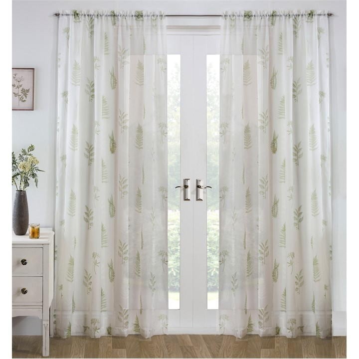 Sheer green voile panel featuring an all-over leaf pattern, elegantly draped over a window with light filtering through, complemented by a white curtain rod.