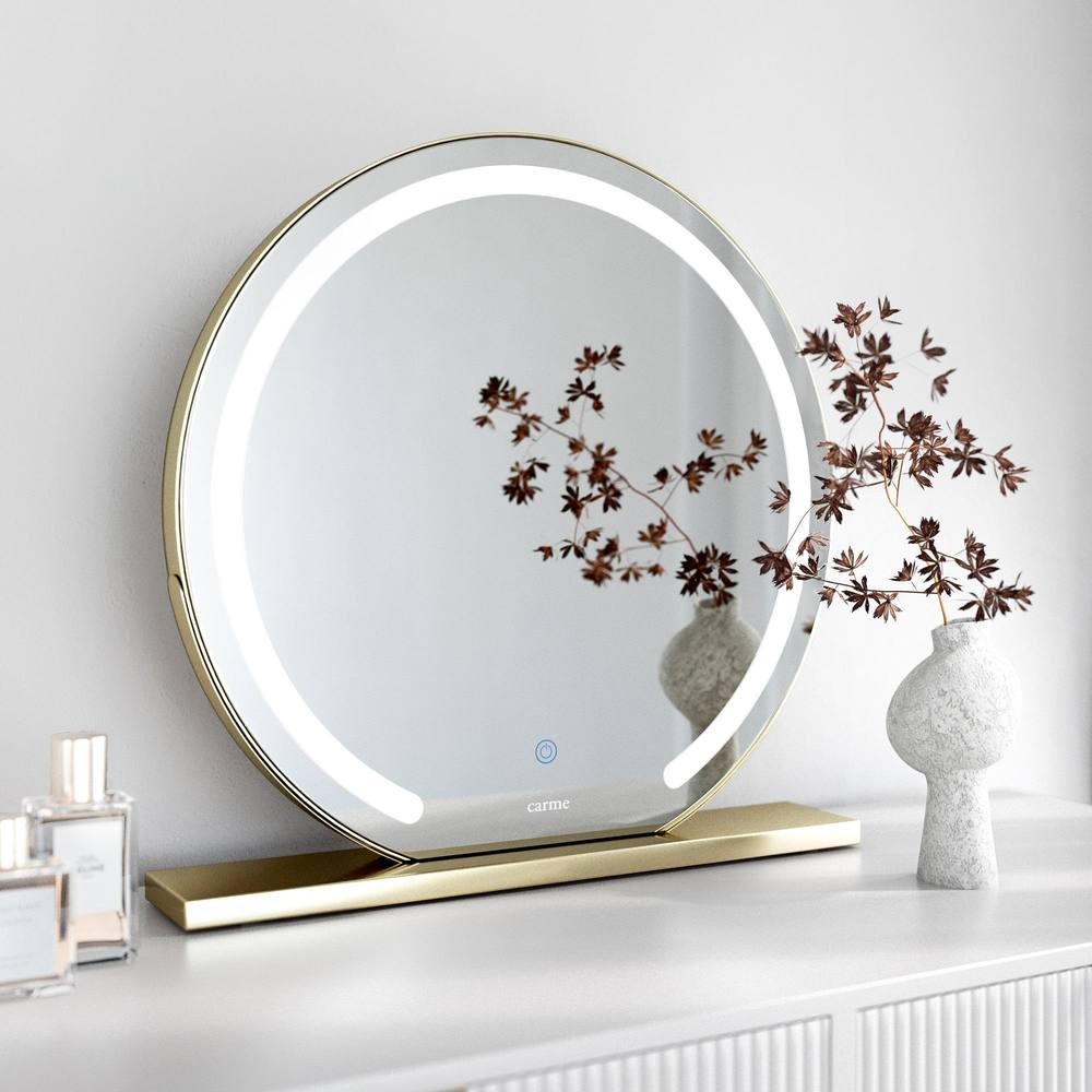 Large round gold touch sensor LED makeup mirror with integrated lights, set on a sleek gold base, reflecting a minimalist decor with a decorative vase and flowers.