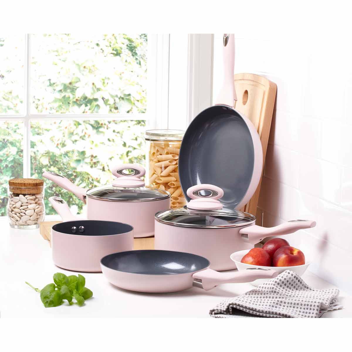 Cermalon Matt Blush Pink 5 Piece Cookware Set featuring two glass lids, non-stick interior, and soft-touch handles, arranged on a kitchen counter with fruits and pasta.