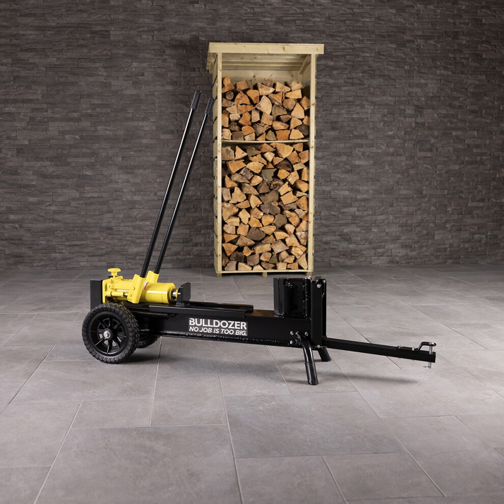 Black hydraulic log splitter with yellow hydraulic pump, large wheels, and a sturdy frame, positioned beside a wooden log storage unit filled with stacked logs.