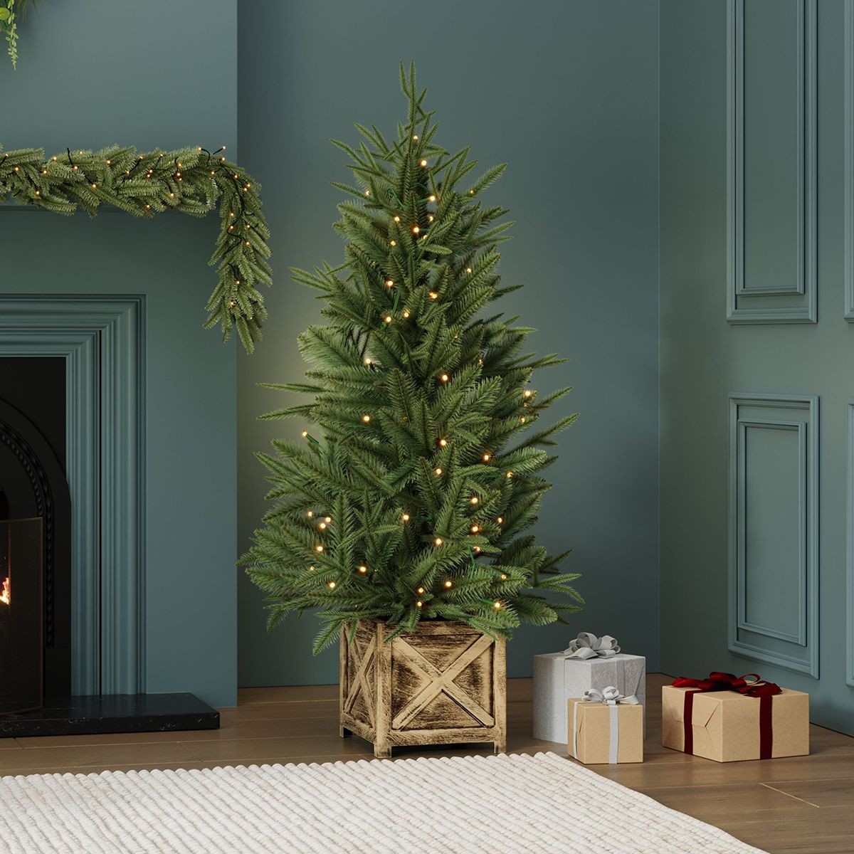 Luxury 4ft pre-lit faux Christmas tree in a rustic box planter, featuring lush green branches and warm white lights, set against a stylish blue wall with holiday gifts nearby.