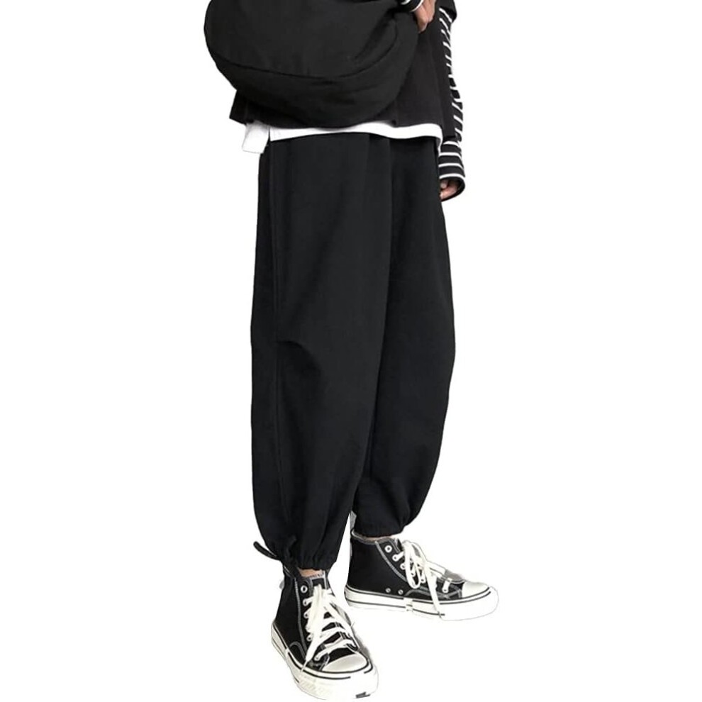 Black, loose-fitting pants with elastic cuffs, styled with a casual white top and black sneakers, featuring a relaxed silhouette and a streetwear aesthetic.