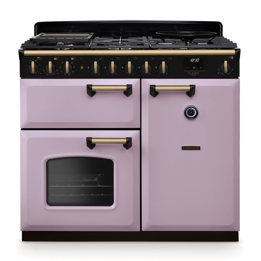 Classic Deluxe 100cm dual fuel range cooker in heather pink and antique brass, featuring a black control panel, six gas burners, and a large glass oven door.