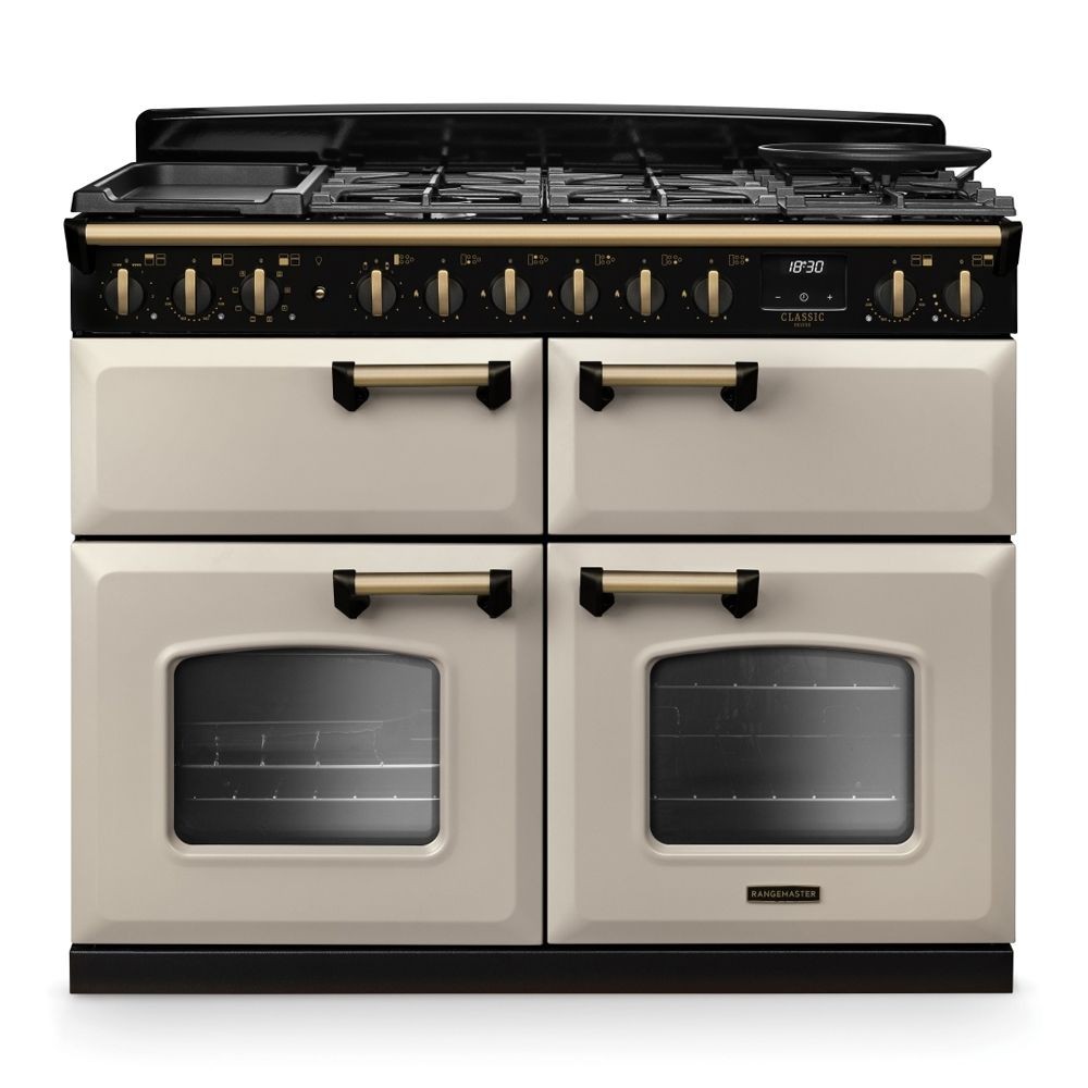 Classic Deluxe 110cm dual fuel range cooker in pale cream with antique brass accents, featuring a five-burner gas hob, two ovens with glass doors, and control knobs.