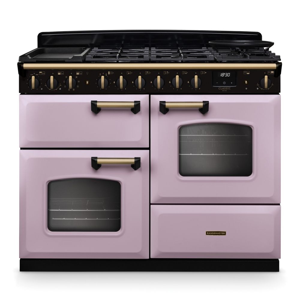 Classic Deluxe 110cm dual fuel range cooker in heather pink and antique brass, featuring a black hob, multiple burners, and two ovens with glass doors and brass handles.
