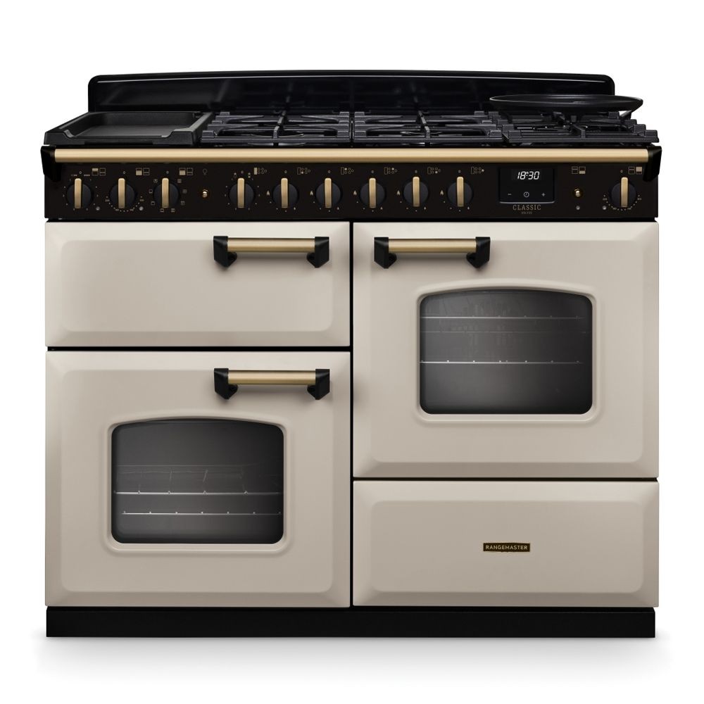 Classic Deluxe 110cm dual fuel range cooker in pale cream with antique brass accents, featuring four gas burners, a griddle, and two ovens with large glass doors.