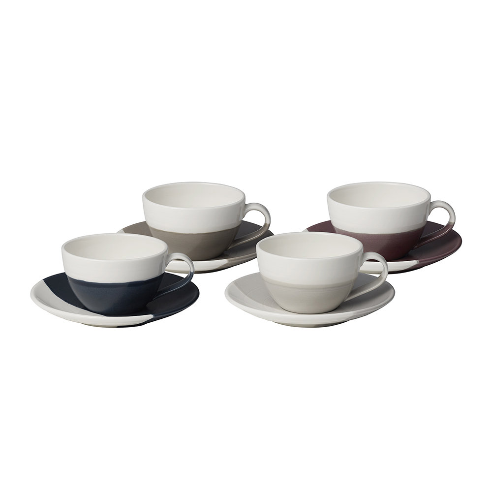 Set of four ceramic flat white cups and saucers in varying colors: navy, taupe, gray, and burgundy, featuring a sleek design with curved handles and contrasting saucer colors.