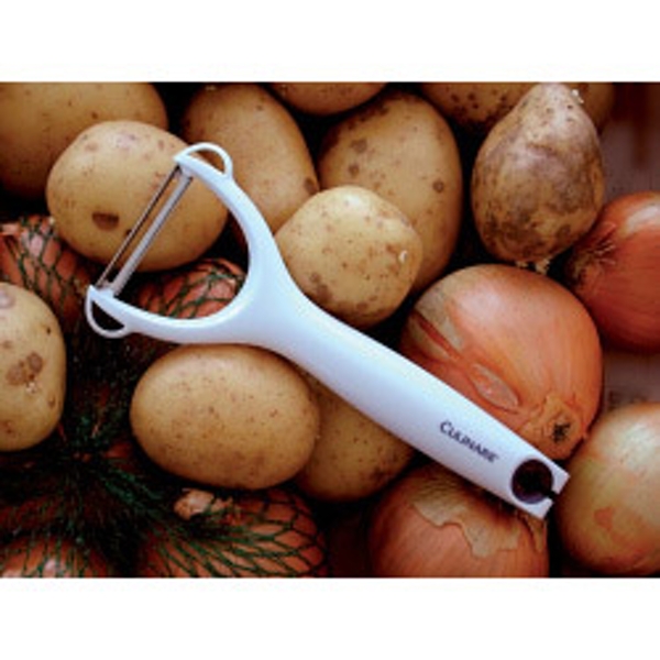 White Culinare Safety Peeler resting on a pile of potatoes and onions, featuring a stainless steel blade and a comfortable grip for easy peeling.
