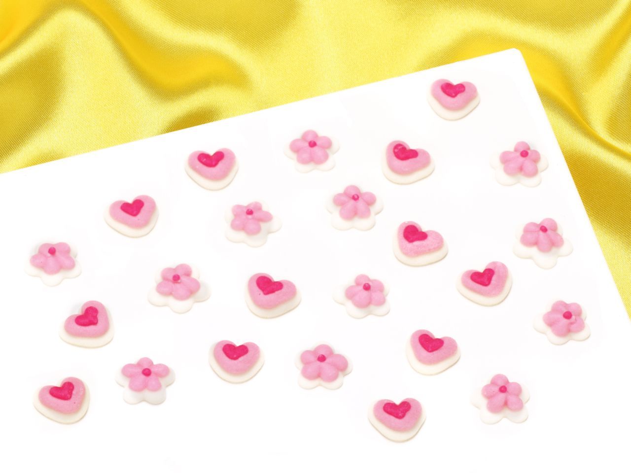Pink mini hearts and flowers sugar pipings made of royal icing, featuring 24 decorative pieces in various designs, set against a yellow satin background.