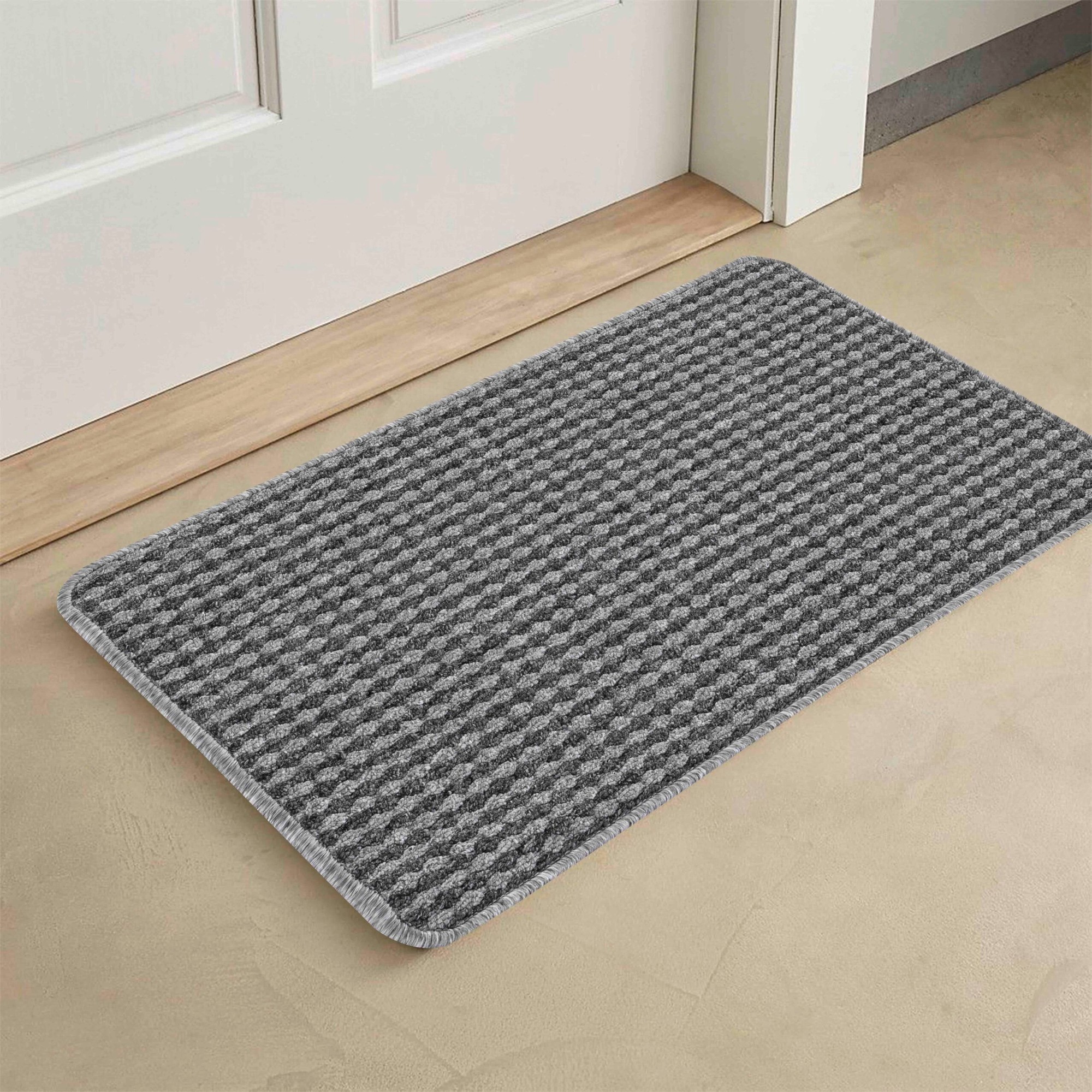 Gray and black striped indoor doormat with a non-slip backing, featuring a textured surface designed to trap dirt, placed near a door on a light-colored floor.