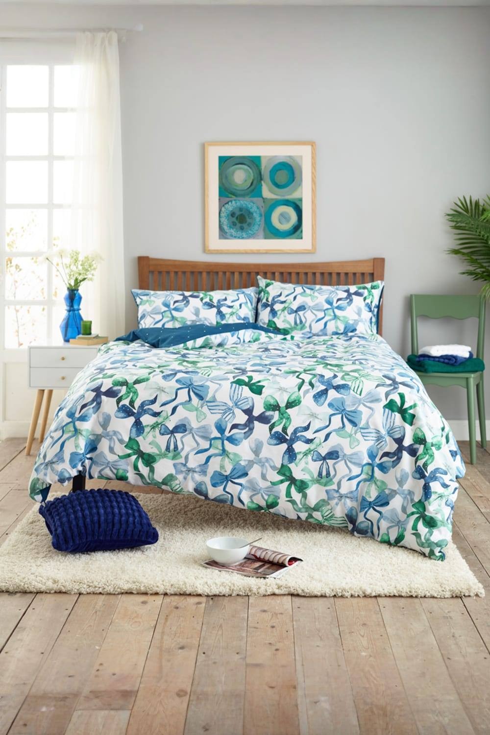 Blue and green Deyongs Bows Print duvet cover set with 200 thread count cotton, featuring a vibrant bow pattern, paired with matching pillowcases, displayed on a wooden bed frame.
