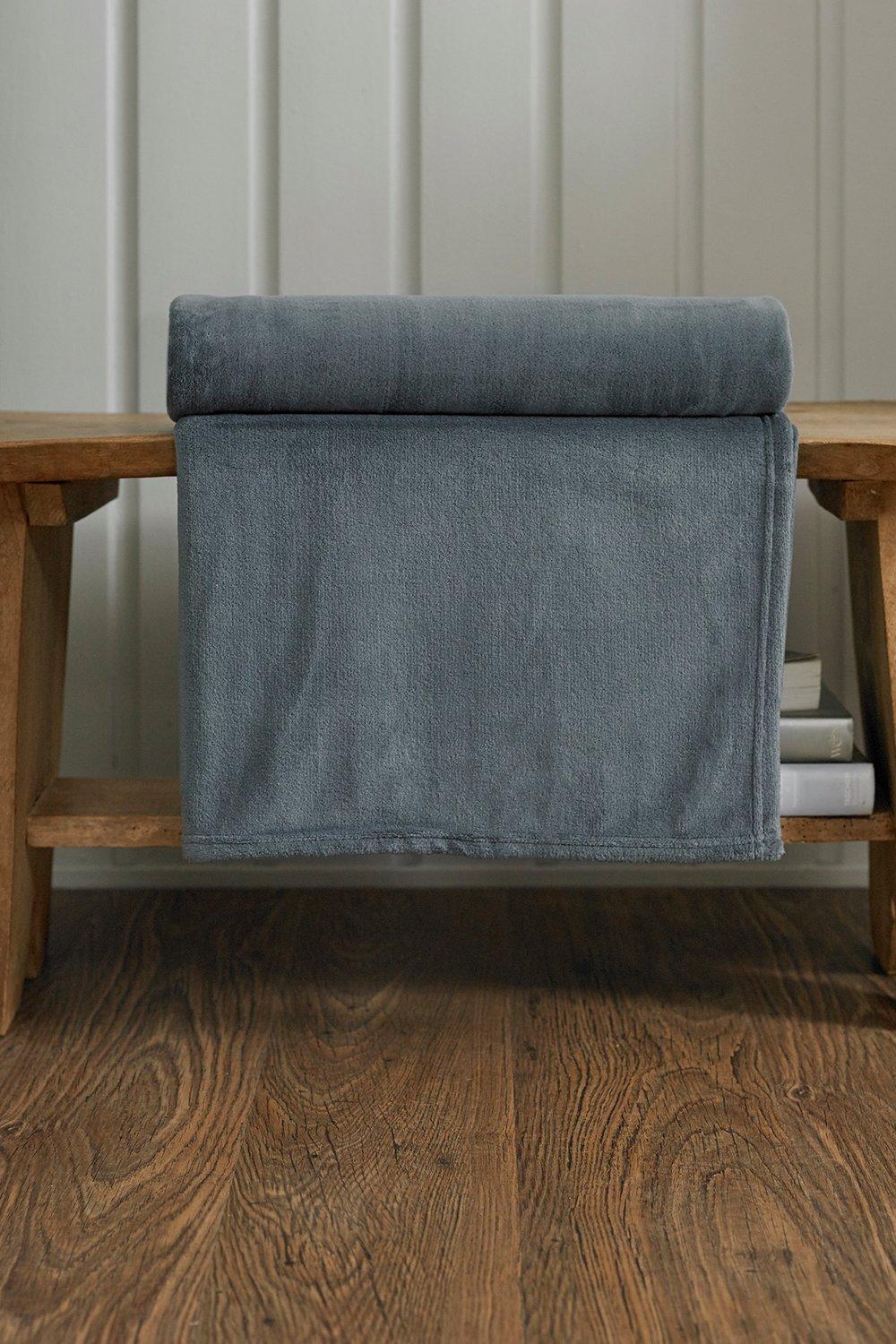 Charcoal-colored luxury throw blanket by Deyongs, featuring an ultra-soft, cozy texture, neatly draped over a wooden bench with books underneath.