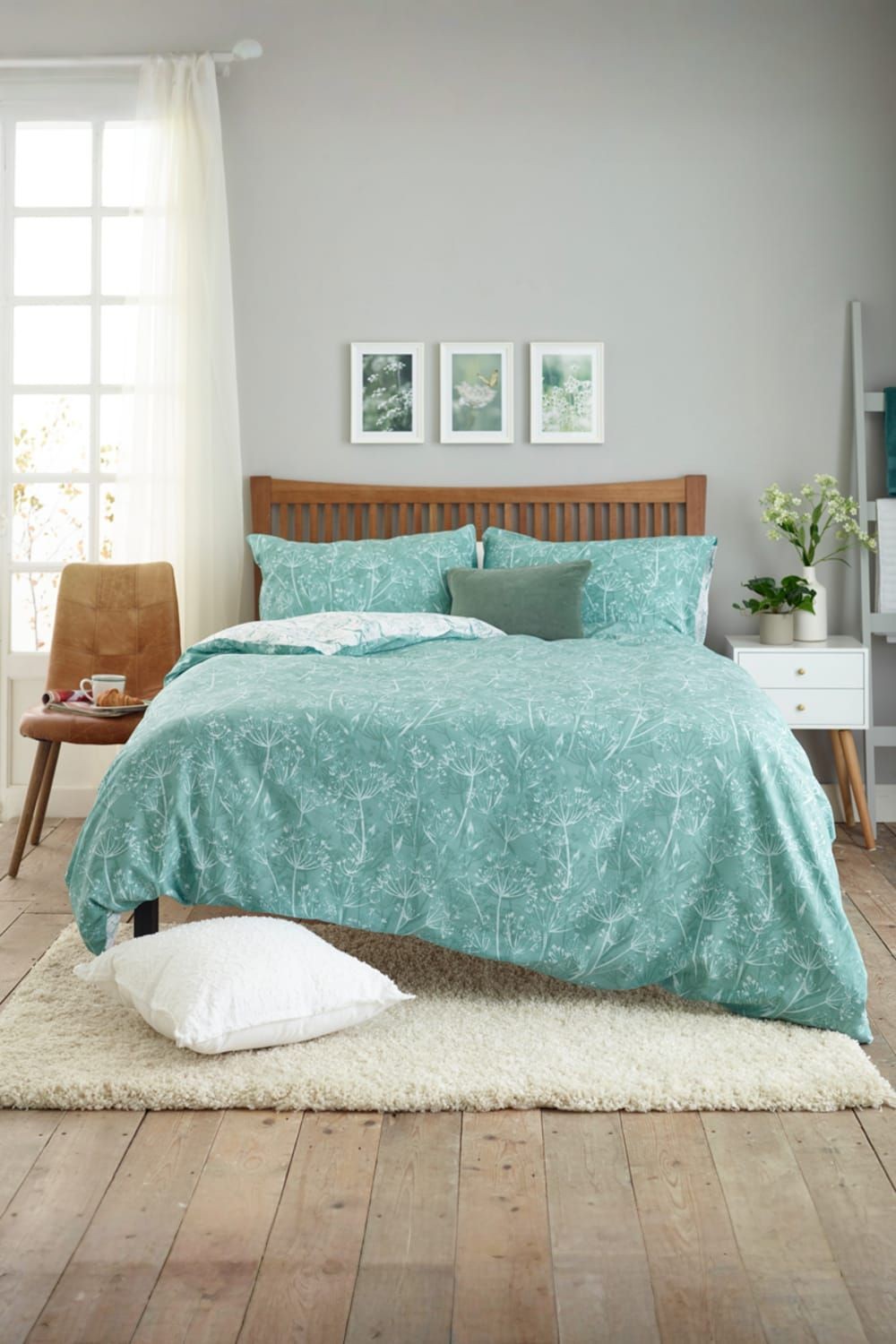 Green cotton-rich duvet cover set with a cow parsley print, featuring a soft texture and 200 thread count, displayed on a wooden bed with matching pillows and a cozy room setting.
