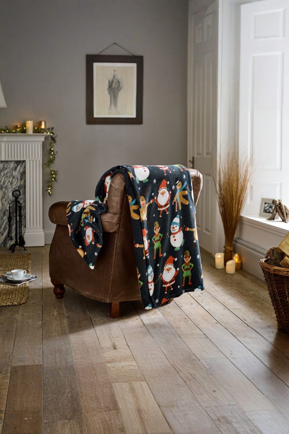Supersoft navy throw blanket featuring festive dancers, snowmen, and elves, measuring 140x180cm, draped over a brown armchair in a cozy living room setting.