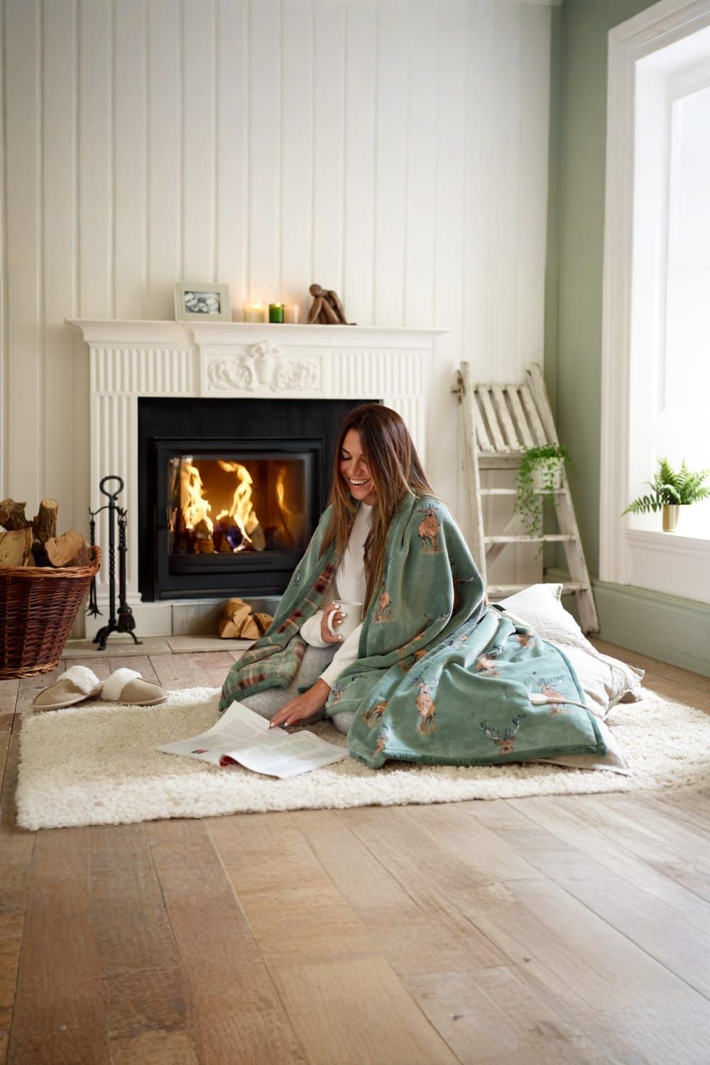 Soft green heated throw blanket featuring a cozy design, measuring 140x180cm, displayed in a warm setting with a fireplace and a woman reading on a plush rug.