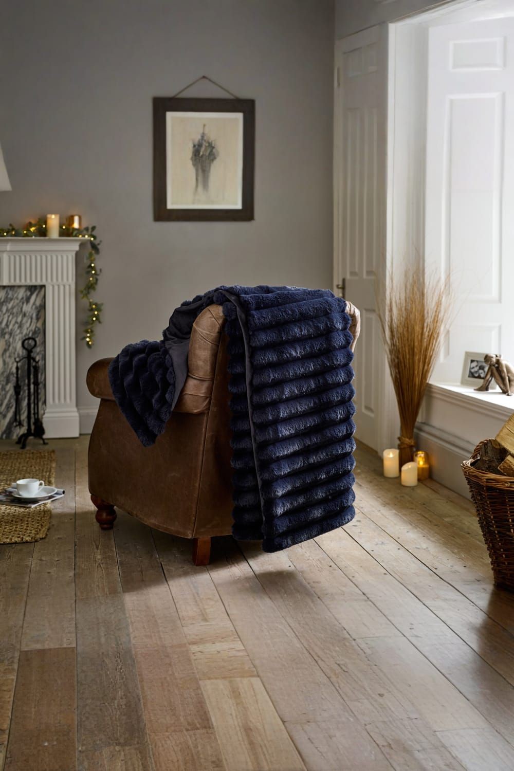Navy plush faux fur throw measuring 130x170cm, featuring a super soft 460gsm texture and a velvety reverse, draped over a brown armchair in a cozy room setting.