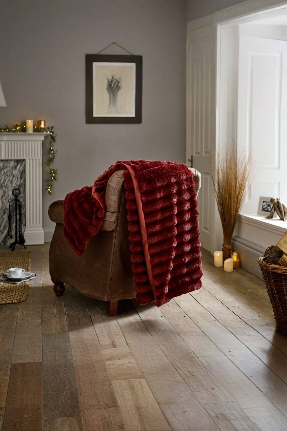 Burgundy plush faux fur throw draped over a brown armchair, featuring a velvety reverse and a luxurious texture, set in a cozy room with wooden flooring and soft lighting.