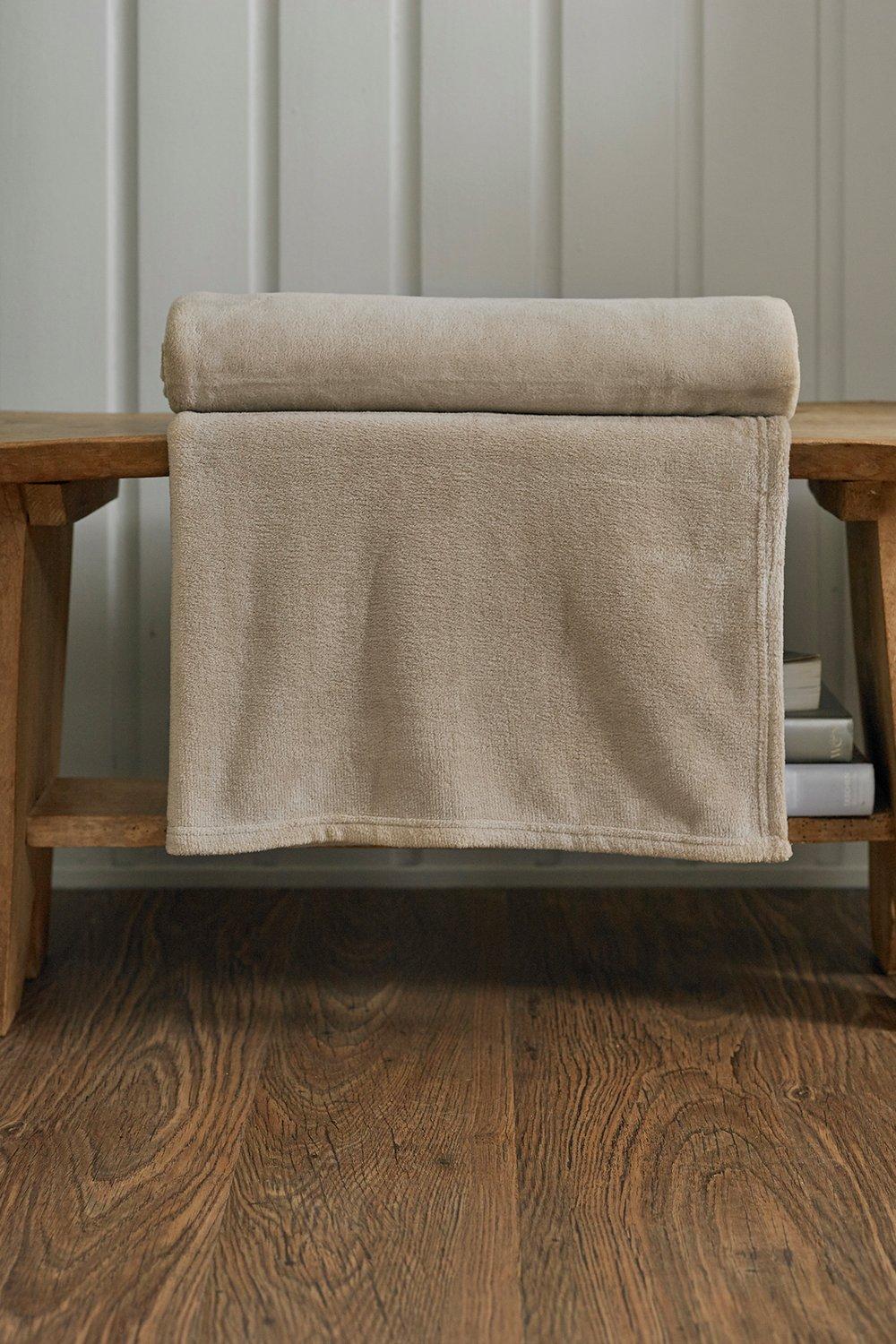 Supersoft beige fleece throw blanket with a smooth texture, neatly rolled and draped over a wooden bench, showcasing its cozy and inviting appearance.