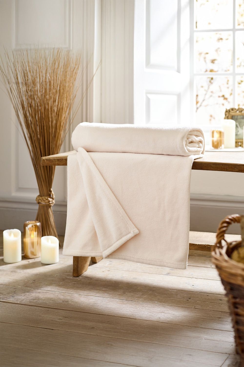 Soft ivory fleece throw draped over a wooden bench, featuring a solid color design and measuring 140cm x 180cm, with candles and decorative elements in the background.