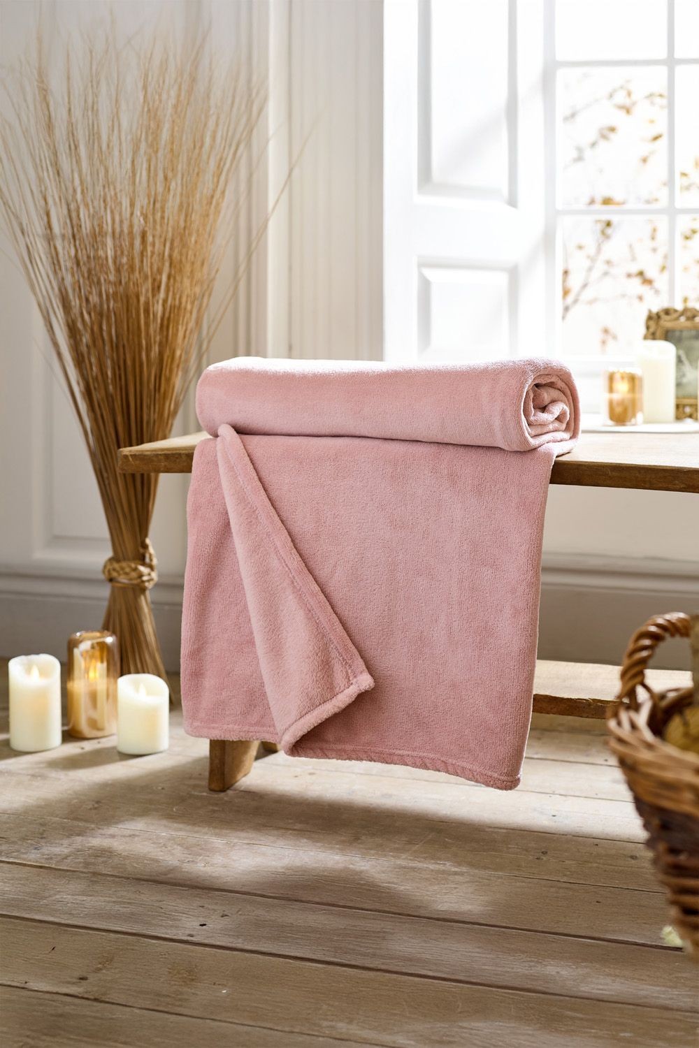 Soft pink fleece throw draped over a wooden bench, showcasing its plush texture; size 140cm x 180cm, ideal for cozying up in any setting.