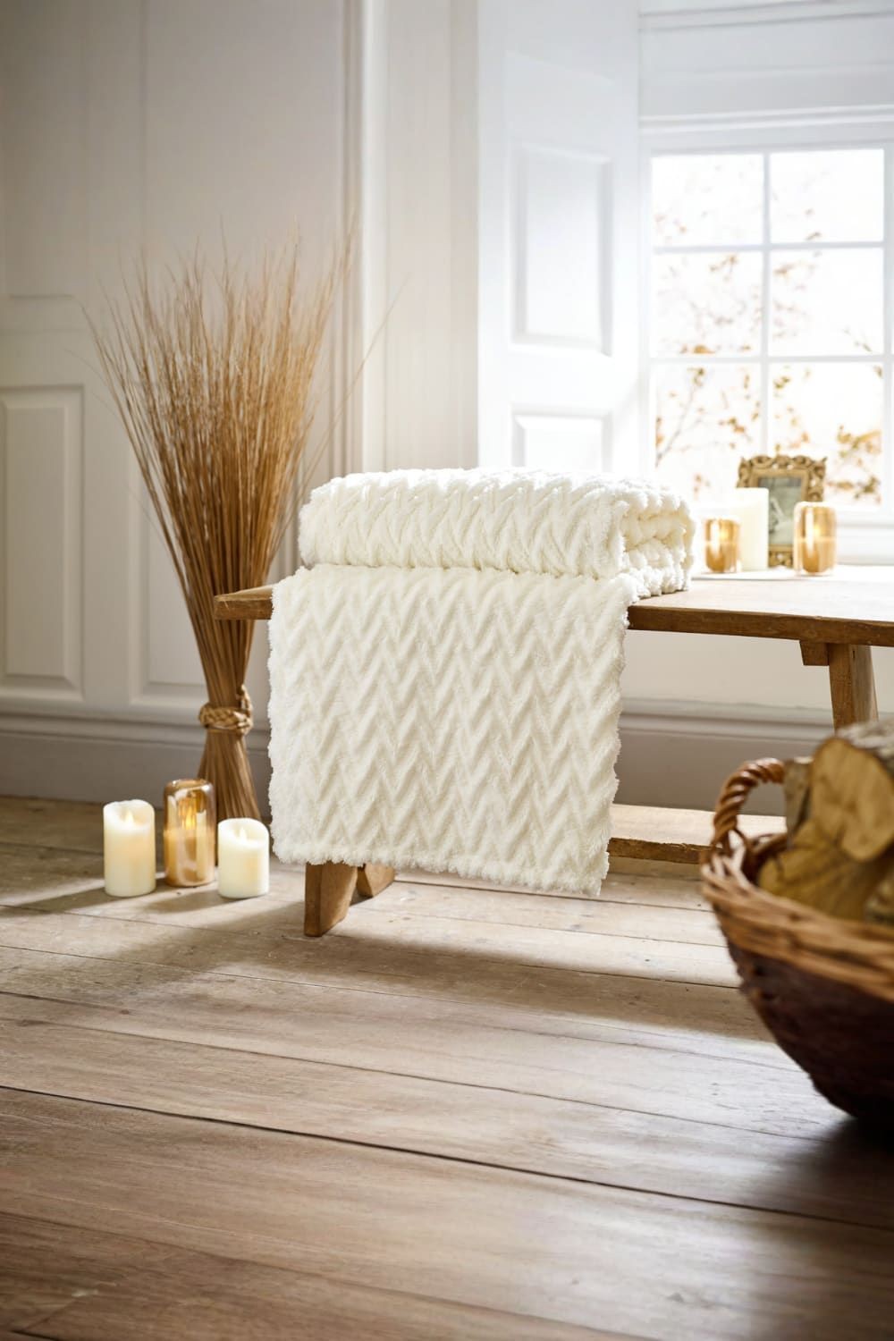 Luxury soft chevron throw in cream, measuring 140x180cm, draped over a wooden bench, with candles and decorative elements in a cozy, well-lit room.