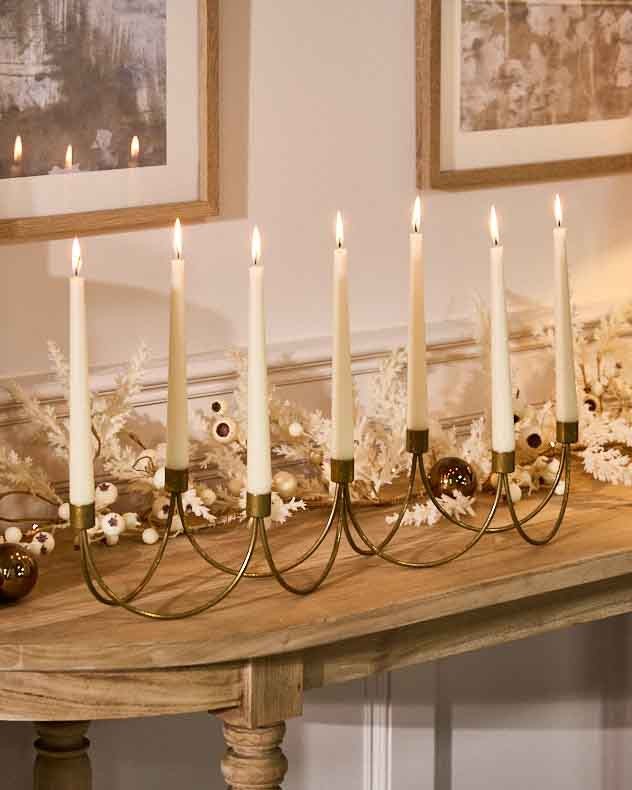 Ornate golden wave candle holder with eight slender cream candles, featuring a wavy design and a polished finish, elegantly displayed on a wooden table.
