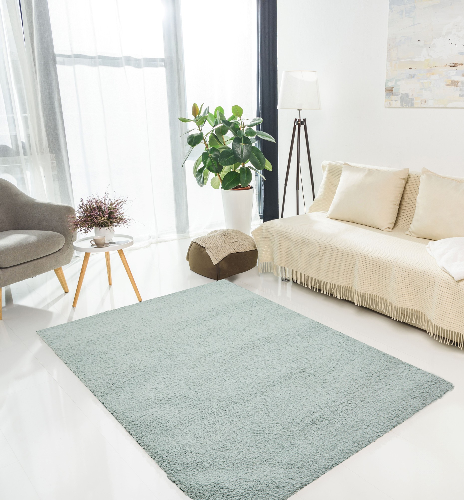 Soft, plush blue area rug with a luxe texture, placed on a bright floor, surrounded by a cozy sofa, a plant, and a modern lamp, enhancing the room's serene ambiance.