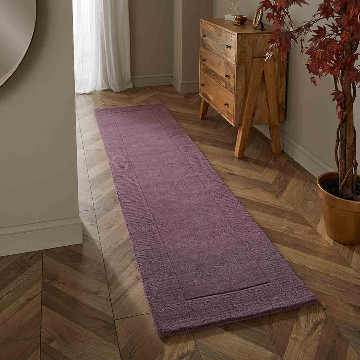 Mauve wool runner measuring 60x230cm, featuring a textured surface and bordered design, placed on a herringbone floor beside a wooden chest and a potted plant.