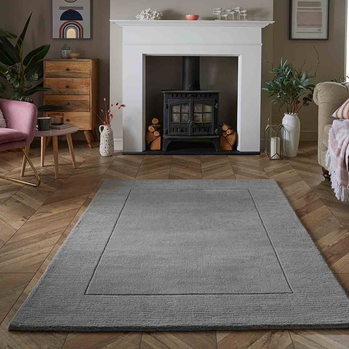 Silver wool rug measuring 160x230cm, featuring a subtle textured design, set on a wooden floor in a cozy room with a fireplace and decorative plants.